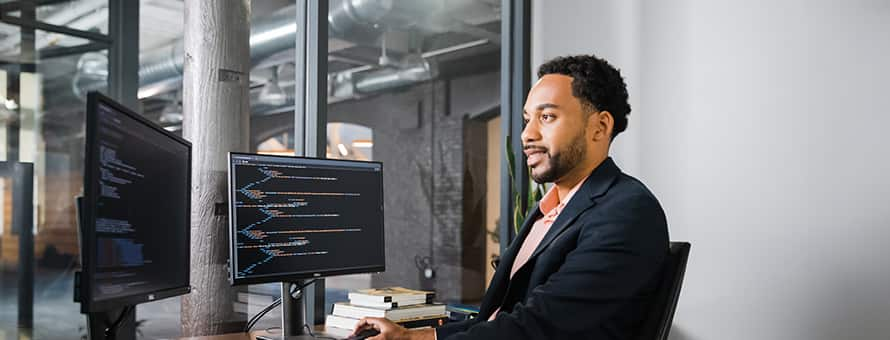 Gary Walker, who earned his degree from SNHU in 2022, wearing dark suit and sitting at a desk with two computer monitors.