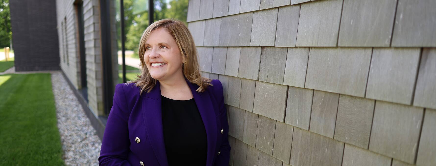 Lisa Marsh Ryerson, president of SNHU, leaning against a wall on campus and wearing a purple blazer
