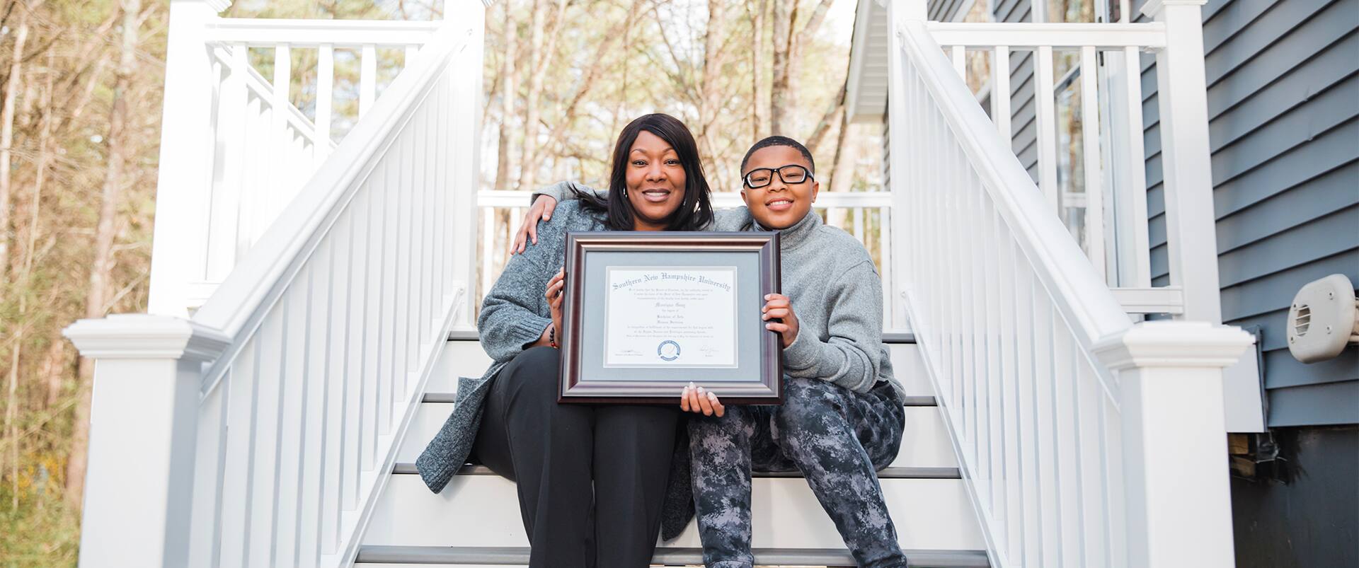 Mo Gray, holding her 2022 online human services degree diploma, while sitting next to her son on a staircase.