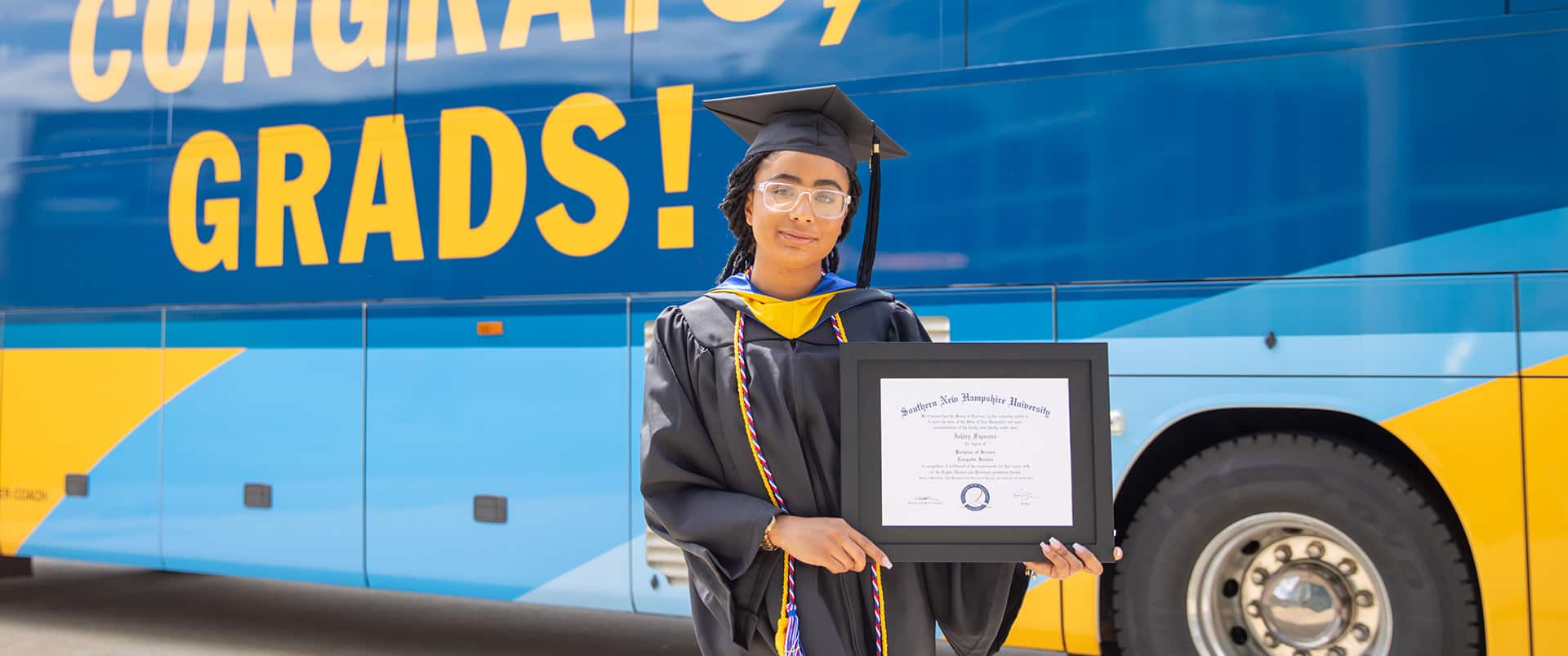 Ashley Figueroa, who earned her computer science degree online, holding her diploma in front of a SNHU bus.