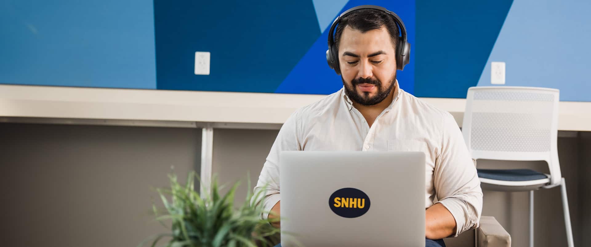 Jesús Súarez, who earned his degree from SNHU in 2021, wearing headphones and working on his laptop that has an SNHU sticker on the front.