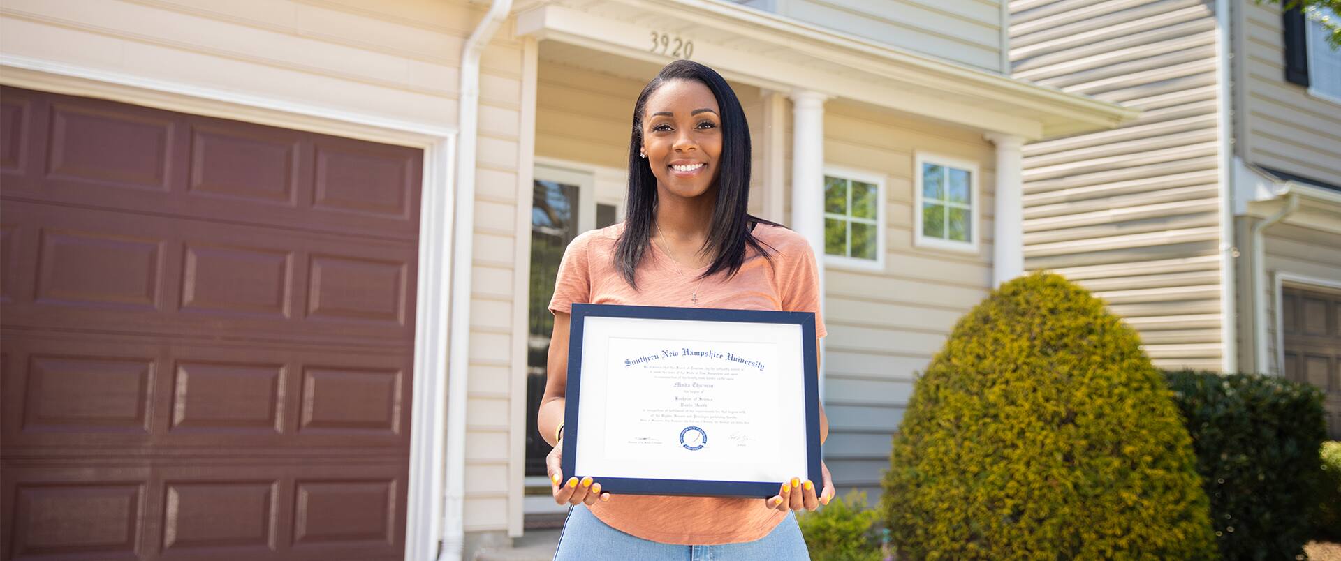 Minda Thurman, who earned her degree from SNHU, standing in front of her home holding her framed.