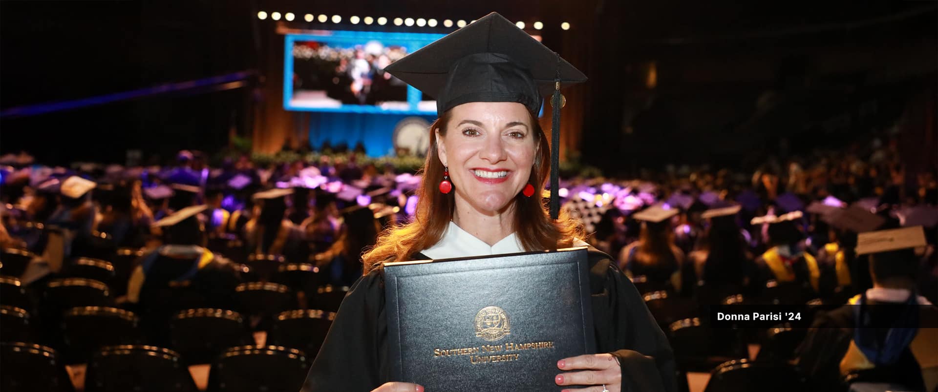Donna Parisi, who earned her master's in English and creative writing in 2024, wearing her cap and gown and holding her diploma.