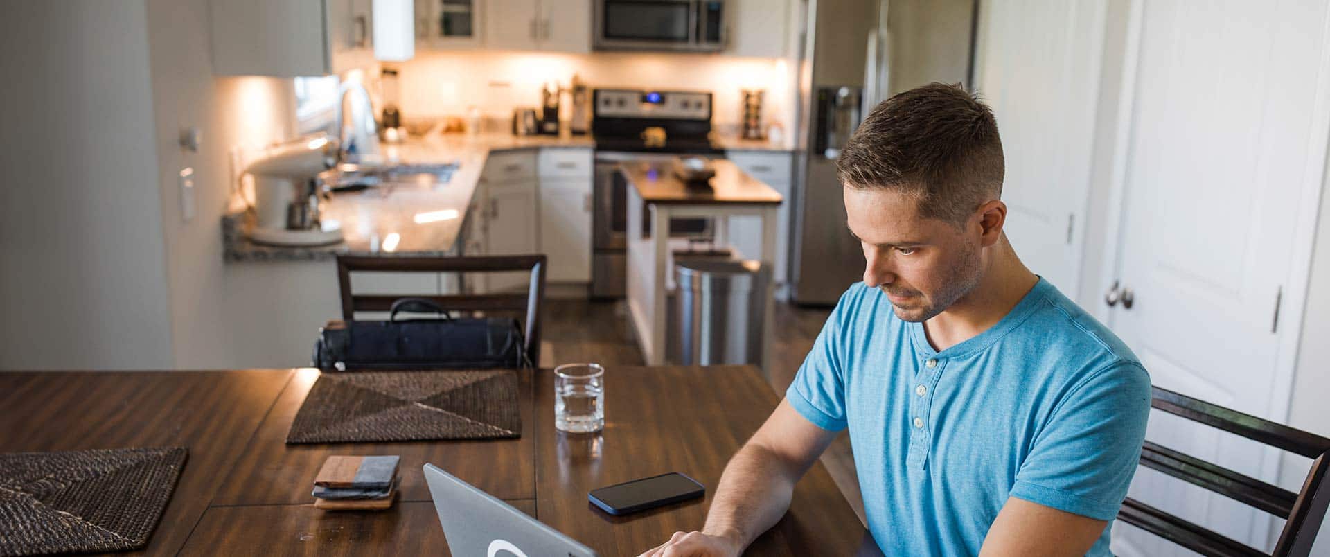 Blake Venable, who earned his degree from SNHU, wearing a blue shirt and sitting at a dining room table typing on a laptop