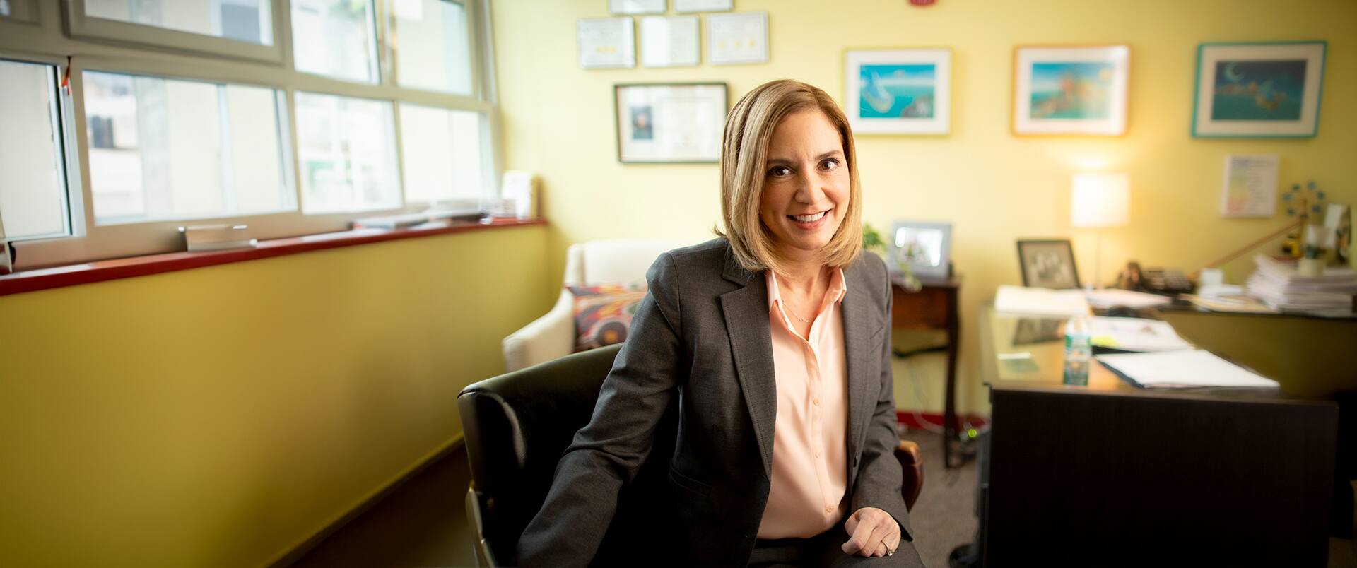 Marti Ilg, who earned her degree from SNHU in 2014, wearing a peach colored blouse and  dark blazer sitting in a swivel chair next to a desk in her office.