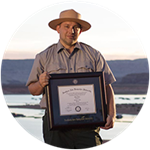 SNHU graduate and Utah resident John Roos wearing a park ranger uniform and holding his framed diploma.