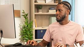 SNHU graduate sitting at a desk using a desktop computer. 